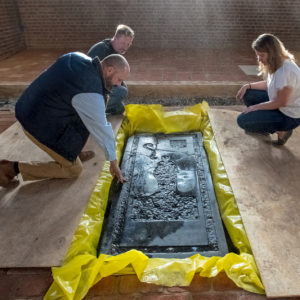 Three staff members crouch around a large tombstone with a figure-shaped inlay