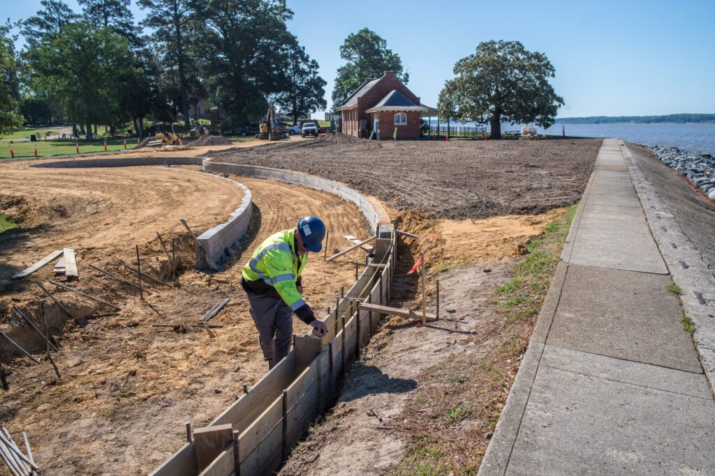 A photo of construction work. A pathway is lined with concrete and ready to be filled in, while a construction worker arranges supports for more concrete lining. It's a sunny day and you can see the Dale House cafe and trees in the background.