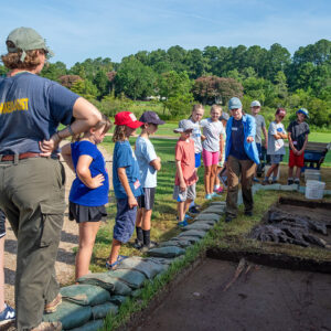 Staff Archaeologist Natalie Reid gives the campers a lay of the land at the cellar site on the first day of camp.