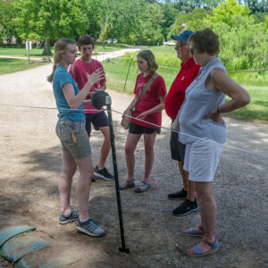 Field School student Katherine Griffith explains the dig at the west "flag" excavations to some visitors.