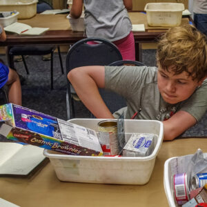 A camper examines the trash of one of the archaeologists on staff, pondering what he can learn about its owner.