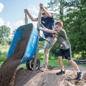Archaeological Intern Dominic Angioletti gives an assist to a camper as he empties screened soil into a pile. The soil will later be used to fill sandbags or backfill excavations.