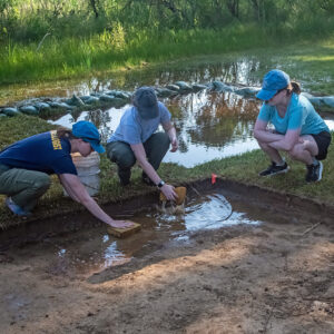 Before they can begin excavations after a flood Staff Archaeologist Natalie Reid and Field School students Ren Willis and Sarah Hespe must soak up water at the clay borrow pit excavations.
