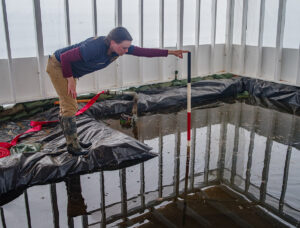 Staff Archaeologist Natalie Reid measures the depth of flooding in the burial structure in Smithfield. Smithfield flooded twice in October. Although the structure was well prepared for a surface flood event, the water instead came in sideways through the soil walls delineating the edges of the excavation area.