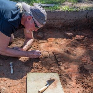 Archaeologist excavating row of bricks