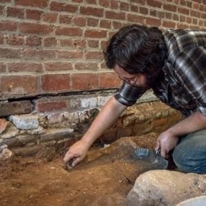 Man excavates dirt under brick wall with trowel and dustpan