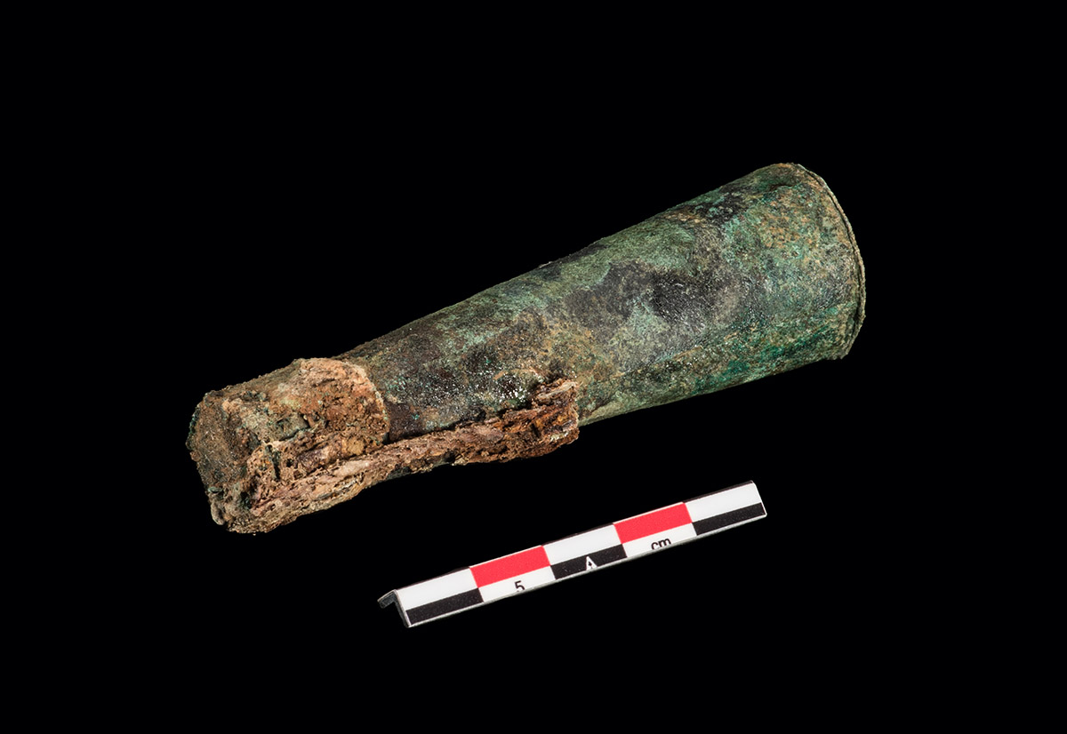 A copper alloy bandolier bottle with surviving cap string. The copper preserved the string as it does with other organic materials.