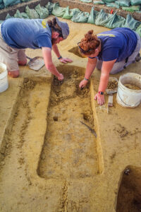 Archaeological Field Technicians Josh Barber and Hannah Barch excavate the top layers of the burial south of the Archaearium.