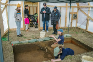 Staff Archaeologist Natalie Reid shares some of the discoveries with visitors in the former burial tent. Archaeological Field Technician Ren Willis is also at work excavating.