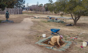 Archaeological Field Technician Josh Barber at excavating in "Pocahontas Plaza". Senior Staff Archaeologist Anna Shackelford and Director of Archaeology Sean Romo are doing GPR work in the cellar at rear.