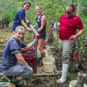 Staff Archaeologist Gabriel Brown, TerraSearch Geophysical's Dr. David Leslie, and field school students Annabel Lawton and Ellie Taylor with a vibracore soil sample taken from the Pitch and Tar Swamp.