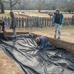 Archaeologists pull tarp over an excavation unit