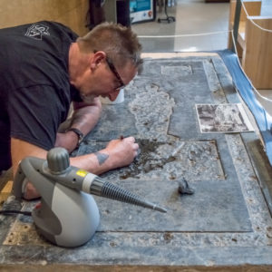 Conservator using a scalpel to scrape glue from a tombstone