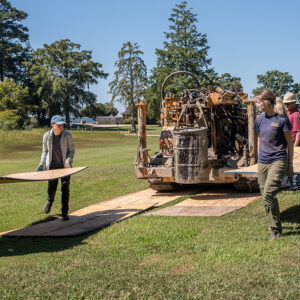 The archaeological staff lays boards in the path of the boring machine so that its tank tracks affects the ground as little as possible.