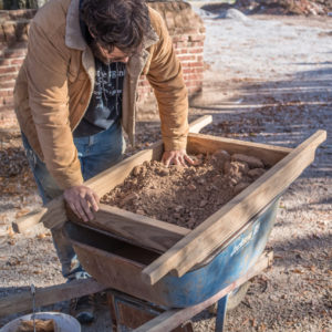 Archaeologist screens dirt into wheelbarrow