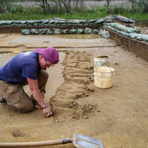 Staff Archaeologist Caitlin Delmas uses her trowel to gently scrape away soil in the clay borrow pit excavations.