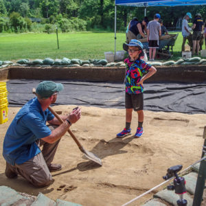 Senior Staff Archaeologist Sean Romo discusses troweling techniques with a camper.