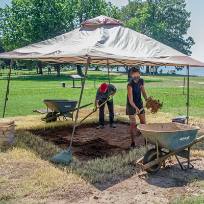 two archaeologists shoveling underneath a tent