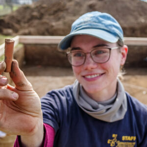 Staff Archaeologist Natalie Reid holds a partial Virginia Indian pipe stem found during the burial excavations.