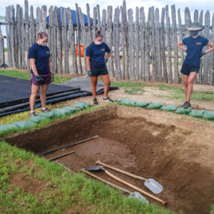 Three archaeologists examine an excavation unit