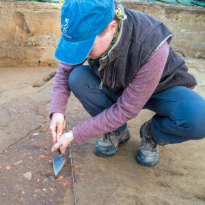 Staff Archaeologist Natalie Reid prepares to excavate a sherd of North Devon gravel-tempered ware found in the excavations west of the Church Tower.