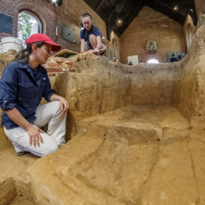 Archaeologist crouches on excavated dirt floor