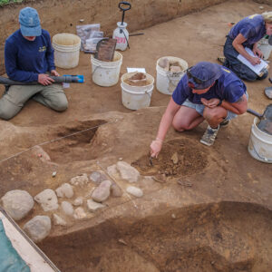 Staff Archaeologists Natalie Reid and Caitlin Delmas and Archaeological Field Technician Katie Griffith at work in the 1607 Burial Ground. Caitlin is excavating cobbles that served as a foundation for a ca. 1611 rowhouse because they will prevent access to the earlier burial beneath them.