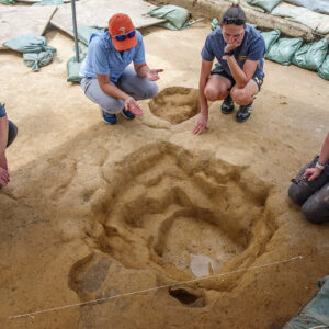 Senior Staff Archaeologists Sean Romo and Mary Anna Hartley, Site Supervisor Anna Shackelford, and Archaeological Field Technician Ren Willis discuss the excavations of one of the subfloor pits in the north field.