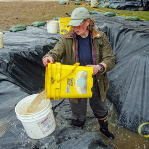 Archaeological Field Technician Eleanor Robb is part of a bucket brigade removing water from the "Tetris Square" after a rainstorm.
