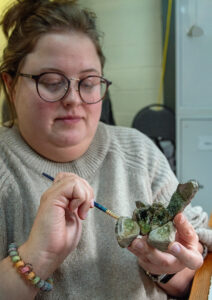 Collections Assistant Lauren Stephens mending a crucible. Glass residue can be seen on the surface, indicating the vessel was used in glass manufacture.