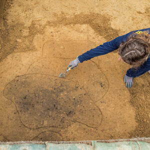 Archaeological Field Technician Ren Willis points to a burn feature found in the excavations outside the Godspeed Cottage.