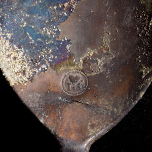 A close up image of the bowl of a tin spoon. A circular mark with a heart flanked by two of the letter "I" is located at the bottom