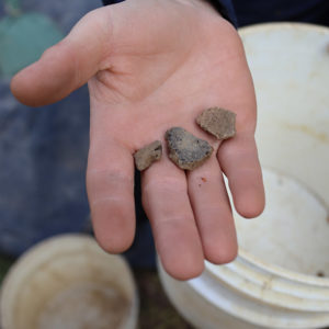 Archaeological Field Technician Jack Schreiber holds Virginia Indian ceramics found north of the Church Tower.