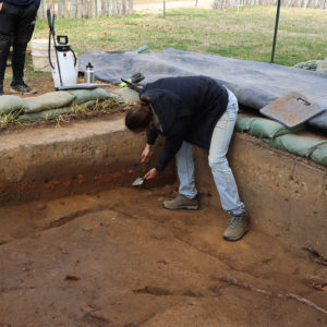 Site Supervisor Anna Shackelford points to the brick rubble layer. White oyster shells can be seen at the lower left.