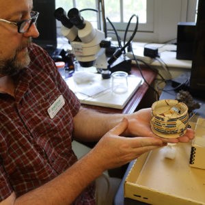 Archaeological Conservator Dr. Chris Wilkins works on a drug jar from the Archaearium that needed repair.