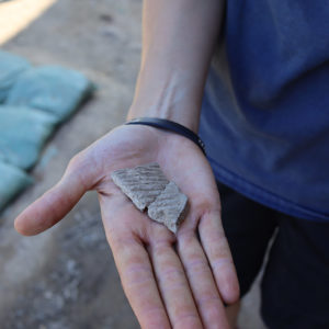 Field Supervisor Anna Shackelford holds two sherds of Virginia Indian pottery found in the excavations north of the Church Tower.