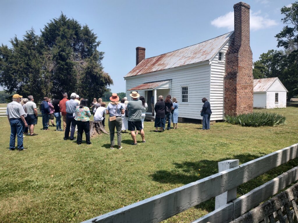 A group of adults listens to a tour guide while standing in front of the restored 1830s slave quarter at Bacon's Castle