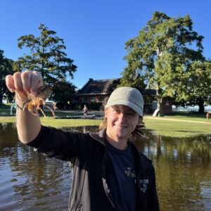 Staff Archaeologist Ren Willis holds a crayfish found in Smithfield. Flooding caused by Hurricane Erin is behind her.