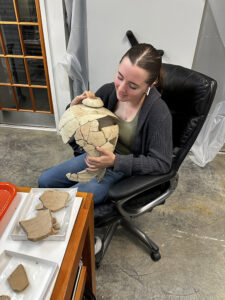 Curatorial Intern Amanda Nedell holds a Spanish coarseware olive jar that she is mending.