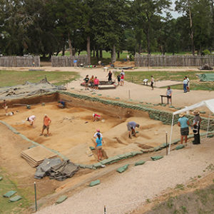 People working and walking around a large excavation site within a palisade