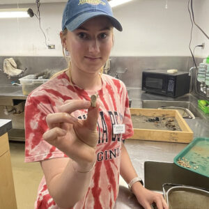 Field School student Janne Wagner holds a partial tobacco pipe with a lion rampant stamped on its heel. This is one of only two pipes in the Jamestown collection bearing a lion decoration. Janne is washing artifacts that have come in from the field.