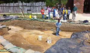 group of children and a guide watch an archaeologist excavating
