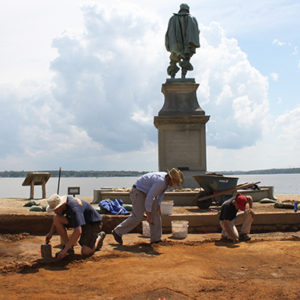 archaeologists excavating behind a statue of John Smith
