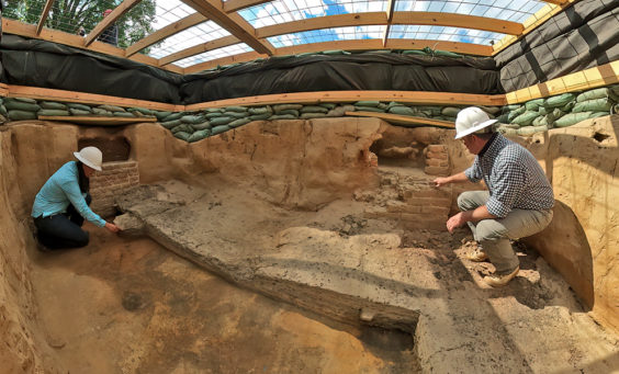two archaeologists kneeling in a large unit covered with a wooden platform