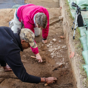 Kalen Anderson and Caitlin Delmas carefully expose plaster associated with the deconstruction of the 1617 Church, which was discarded in the churchyard.