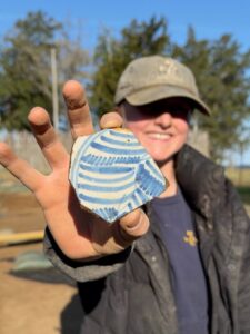 Archaeological Field Technician Katie Griffith holds a sherd of Portuguese faience she found in the well's clay cap.