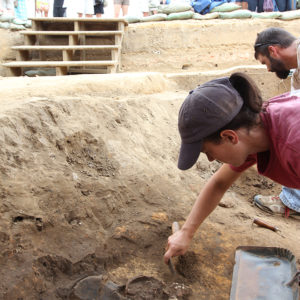archaeologist using a trowel to clean soil from around buried human bones