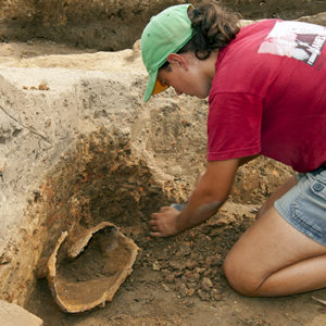 archaeologist kneeling next to an in situ corroded helmet