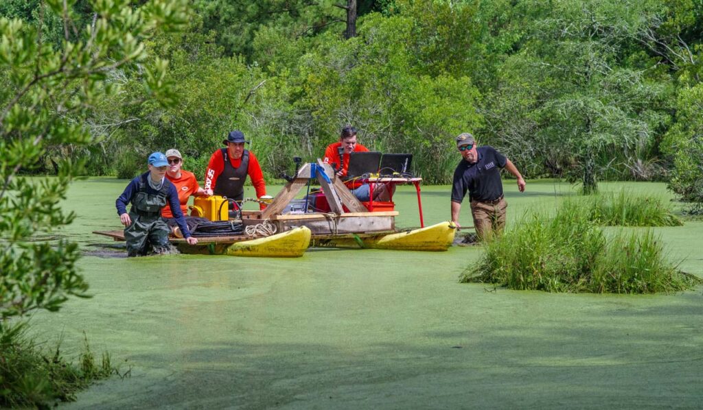 A group of people push the survey float across the swamp