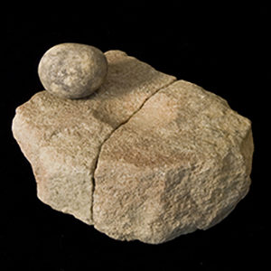 Cracked stone with round indentation in middle and small round stone sitting on top